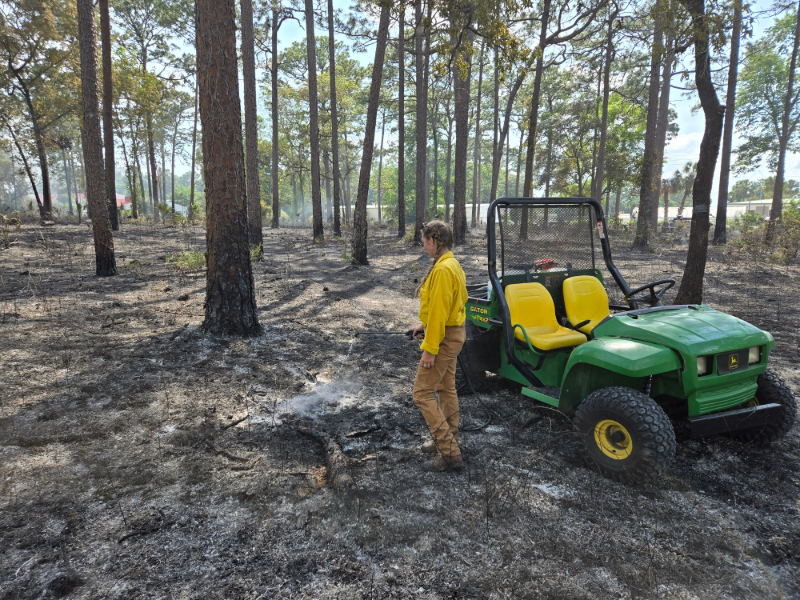 a girl using a hose to put out embers after a prescribed burn