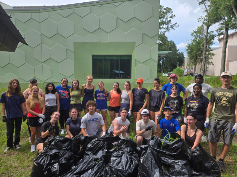 a group of students standing behind trash bags full of invasive weeds